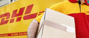 Ein Mitarbeiter des Paketdienstleisters DHL der Deutschen Post trägt ein Paket (Symbolbild).