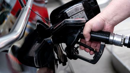 Ein Mann hält eine Zapfpistole an einer Tankstelle in der Hand.