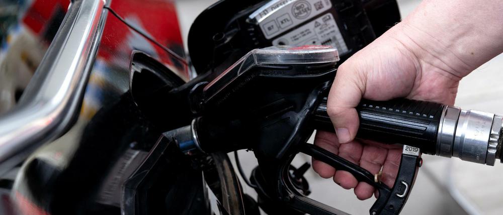 Ein Mann hält eine Zapfpistole an einer Tankstelle in der Hand.