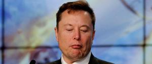 Elon Musk schaut bei einem Gespräch auf sein Smartphone.