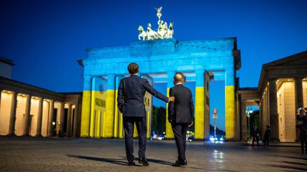 Bundeskanzler Olaf Scholz und Frankreichs Präsident Emmanuel Macron vor dem in den ukrainischen Farben beleuchteten Brandenburger Tor. A