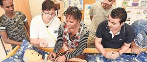 Junge Interessent:innen an einer Altenpflegehelferausbildung stehen um ein Krankenbett mit einer Puppe herum und üben Handgriffe am Patienten.