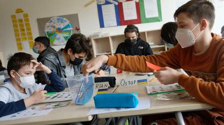 Schüler aus der Ukraine, zu erkennen an ihren Namensschildern mit der ukrainischen Flagge, sitzen in einem Klassenraum und bearbeiten Arbeitsbögen.