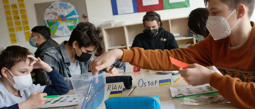 Schüler aus der Ukraine, zu erkennen an ihren Namensschildern mit der ukrainischen Flagge, sitzen in einem Klassenraum und bearbeiten Arbeitsbögen.