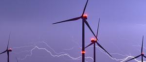 Ein Blitz erhellt den Nachthimmel über Windenergieanlagen mit roten Positionslichtern. 