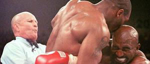 Der Moment danach. Evander Holyfield (rechts) verzieht das Gesicht vor Schmerz, nachdem ihm Mike Tyson einen Teil des rechten Ohres abgebissen hat.