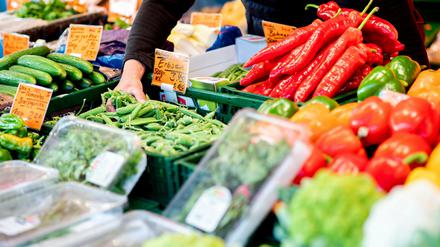 Ein Verkäufer greift an einem Obst- und Gemüsestand auf dem Wochenmarkt in eine Kiste mit Erbsen
