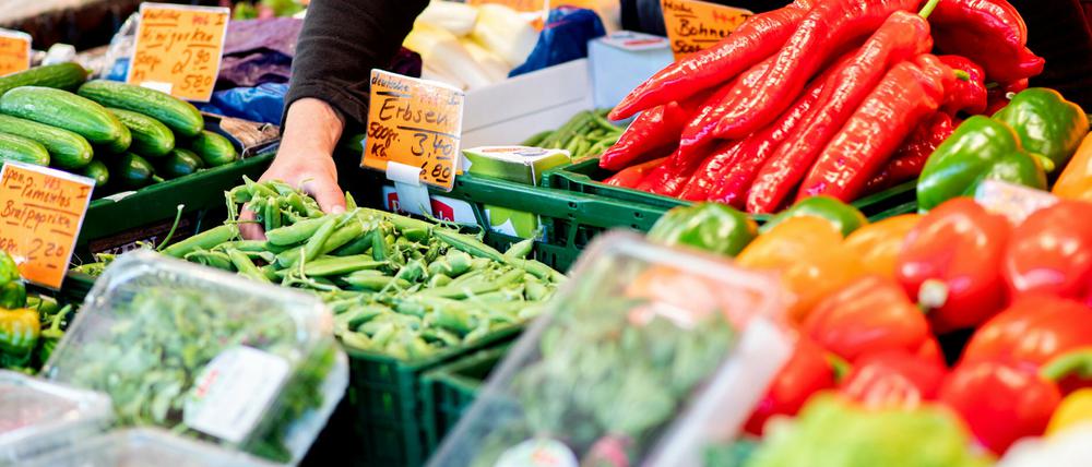 Ein Verkäufer greift an einem Obst- und Gemüsestand auf dem Wochenmarkt in eine Kiste mit Erbsen
