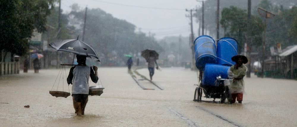 Menschen waten durch eine überschwemmte Straße in Bangladesch (Symbolbild).