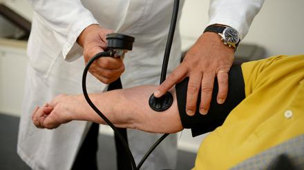 Ein Hausarzt misst in seiner Praxis einer Patientin den Blutdruck. 
