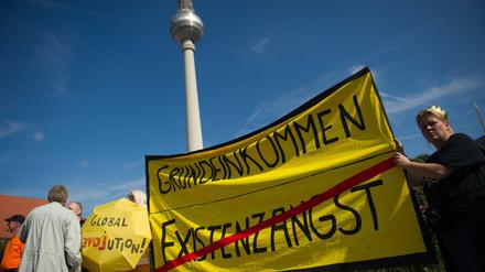 Teilnehmer einer Demonstration für ein bedingungsloses Grundeinkommen vor dem Fernsehturm mit einem Transparent mit dem Aufdruck Grundeinkommen.