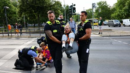 Eine Aktivistin der Letzten Generation wird von Polizisten von der Straße getragen. 