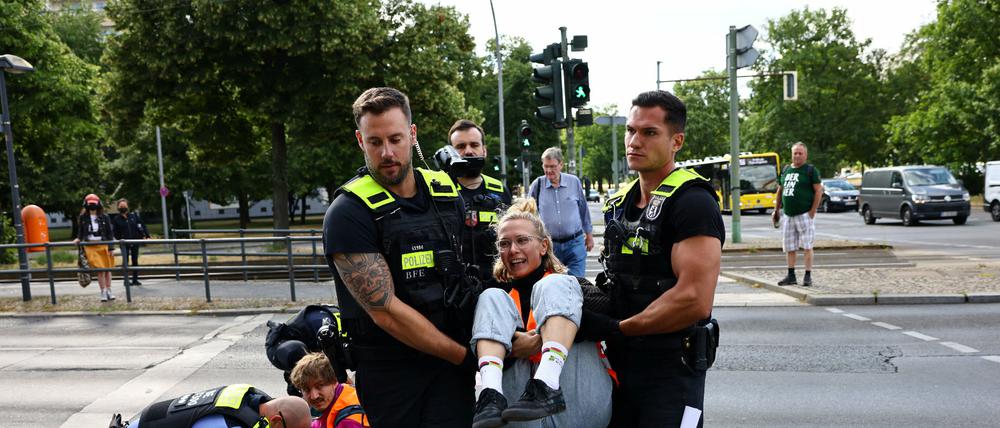 Eine Aktivistin der Letzten Generation wird von Polizisten von der Straße getragen.