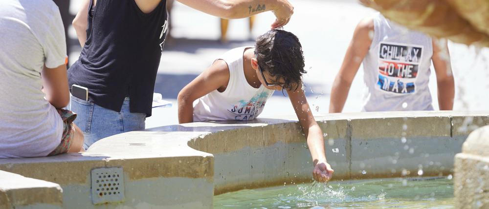 Eine Mutter gießt während einer Hitzewelle ihrem Sohn Wasser über den Kopf am Brunnen auf dem Platz Virgen de los Reyes in Sevilla. Foto: dpa/Joaquin Corchero/EUROPA PRESS
