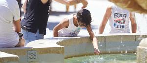 Eine Mutter gießt während einer Hitzewelle ihrem Sohn Wasser über den Kopf am Brunnen auf dem Platz Virgen de los Reyes in Sevilla. Foto: dpa/Joaquin Corchero/EUROPA PRESS