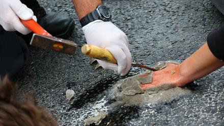 Mit Hammer und Stemmeisen löst ein Polizeibeamter die festbetonierte Hand eines Demonstranten vom Asphalt der Autobahnausfahrt ab.