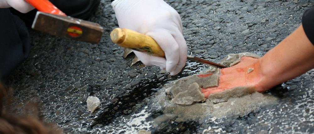 Mit Hammer und Stemmeisen löst ein Polizeibeamter die festbetonierte Hand eines Demonstranten vom Asphalt der Autobahnausfahrt ab.