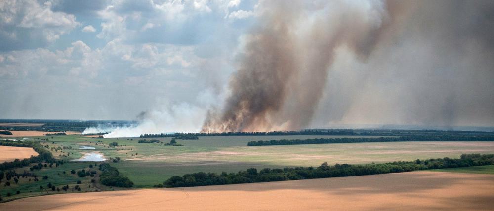 04.07.2022, Ukraine, Dnipropetrovsk: Rauch steigt von den Frontlinien auf, an denen sich ukrainische und russische Truppen heftige Kämpfe liefern, während zehn Kilometer davon entfernt, in der Region Dnipropetrowsk, Landwirte ihre Felder ernten.