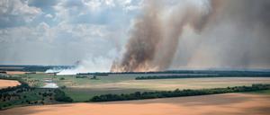 04.07.2022, Ukraine, Dnipropetrovsk: Rauch steigt von den Frontlinien auf, an denen sich ukrainische und russische Truppen heftige Kämpfe liefern, während zehn Kilometer davon entfernt, in der Region Dnipropetrowsk, Landwirte ihre Felder ernten.