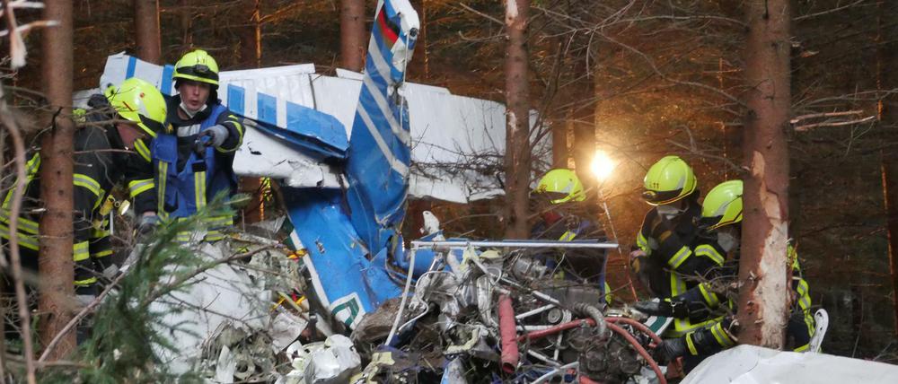 Einsatzkräfte arbeiten am Wrack eines kleinen Flugzeugs, das in ein Waldgebiet gestürzt ist.