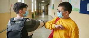 Cheerful elementary students waiting in a school hall before class starts while wearing protective face mask during COVID-19 pandemic