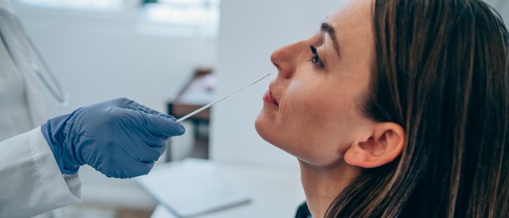 Shot of a doctor using cotton swab while doing coronavirus PCR test at the hospital. Doctor laboratory assistant takes swab from nose of sick patient. Unrecognizable doctor with protective glove taking coronavirus sample from female patient's nose.