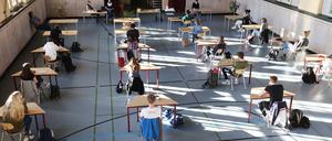 Schüler mit Mundschutz sitzen bei der Prüfungsvorbereitung fürs Abitur in einer zum Schulraum umfunktionierten Turnhalle.