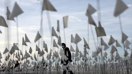 LOS ANGELES, CALIFORNIA - NOVEMBER 18: A person wearing a face covering walks past a white flag memorial installation outside Griffith Observatory honoring the nearly 27,000 Los Angeles County residents who have died from COVID-19 on November 18, 2021 in Los Angeles, California. Los Angeles is holding a three-day citywide �Strength and Love� memorial honoring those who died and those who �have held the city together throughout the pandemic� including first responders and essential workers. Los Angeles County reported 26 additional deaths due to COVID-19 today.   Mario Tama/Getty Images/AFP (Photo by MARIO TAMA / GETTY IMAGES NORTH AMERICA / Getty Images via AFP)