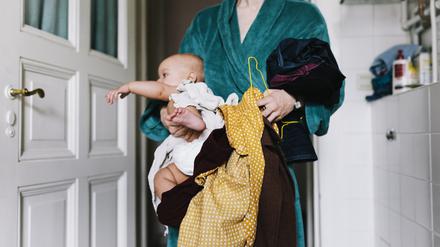 A single mother with her baby trying to get dressed in the morning, carrying clothes to get changed.