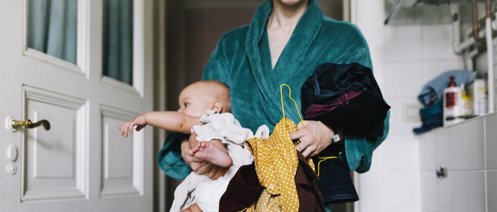 A single mother with her baby trying to get dressed in the morning, carrying clothes to get changed.