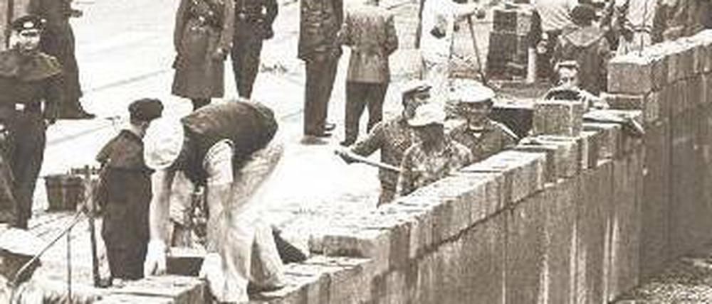 Es geschah in Berlin: Bewacht von Volkspolizisten, mussten Maurer am 13. August 1961 die Steine für das sozialistische Schandwerk zusammenfügen.