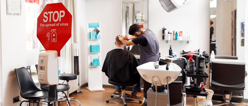 Der Friseur Noor Agha Karimi frisiert einen Kunden in dem Friseursalon Mac Hair in Wannsee. In Salon steht ein Schild mit der Aufforderung, die Hände zu desinfizieren. Angesichts der Omikron-Welle hat der Berliner Senat einige neue Corona-Regeln beschlossen. Die Verordnung ist seit dem 05.02.2022 in Kraft. +++ dpa-Bildfunk +++