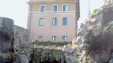 Schmucklos am Hang. Doch Benedikts Ausblick von seiner Heimstatt wird von der palmenumringten bronzenen Petrusstatue schräg unter ihm über die zum Greifen nahe Kuppel des Petersdoms über die ganze Stadt reichen.