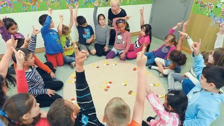 Die Leiterin der Herman-Nohl-Schule aus Britz, Ilona Bernsdorf, sitzt mit Kindern einer Jül-Klasse an einem Mathelernteppich.