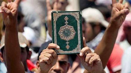 Demonstranten halten einen Koran in die Luft.