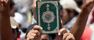 Demonstranten halten einen Koran in die Luft.