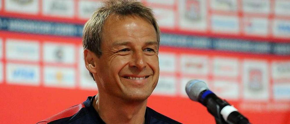 Jürgen Klinsmann sitzt grinsend auf einer Pressekonferenz