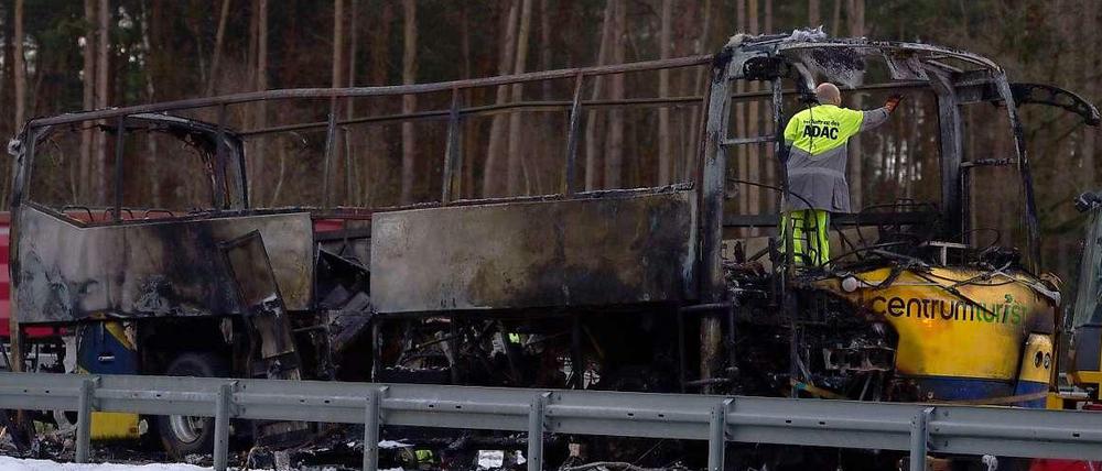 Ein Mitarbeiter des ADAC steht am Montag auf der Autobahn 13 nahe Ortrand (Brandenburg) in einem ausgebrannten dänischen Reisebus.