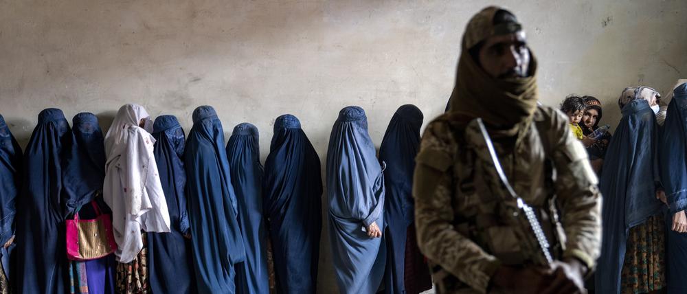 Ein Taliban-Kämpfer steht Wache, während Frauen bei der Lebensmittelverteilung warten.