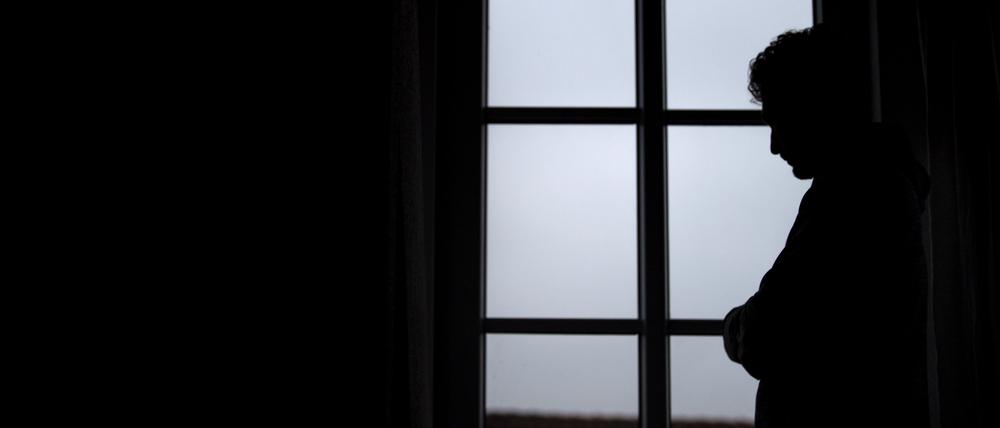 Ein Mann steht am Fenster seiner Wohnung. (Symbolbild, gestellte Szene)