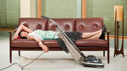 1950's housewife  with apron, napping on mid-sentury modern couch with Retro Hoover vacume cleaner