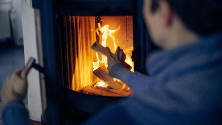 Eine Frau wirft ein Holzscheit in einen Kaminofen.