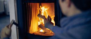 Eine Frau wirft ein Holzscheit in einen Kaminofen. 