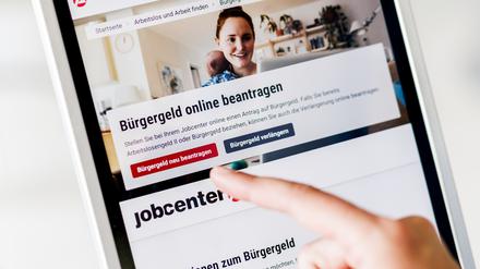 Eine Frau tippt auf einem Tablet auf einen Link zum Beantragen des Bürgergeldes im Kundenbereich im Jobcenter Berlin Mitte. 