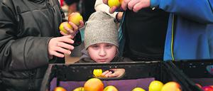 16.03.2022, Berlin: Ein Kind schaut über eine Kiste mit Äpfeln, während ihre Eltern, Kriegsflüchtlinge aus der Ukraine, Lebensmittel an der Essenausgabe holen in der "Welcome Hall Land Berlin", der ersten Anlaufstelle nach der Ankunft der Flüchtlinge auf dem Berliner Hauptbahnhof. In Berlin werden weiter steigende Zahlen von Flüchtlingen aus der Ukraine erwartet. Foto: Carsten Koall/dpa +++ dpa-Bildfunk +++