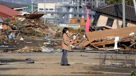 Eine Frau steht vor zerstörten Gebäuden in Soma, Fukushima.