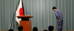 Der japanische Premierminister verbeugt sich vor Beginn einer Pressekonferenz vor der mit Trauerflor geschmückten Nationalflagge.