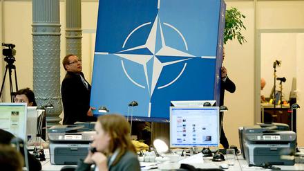 Wohin bloß? Mitarbeiter des Auswärtigen Amtes tragen ein Schild mit dem Nato-Logo durch das Pressezentrum.