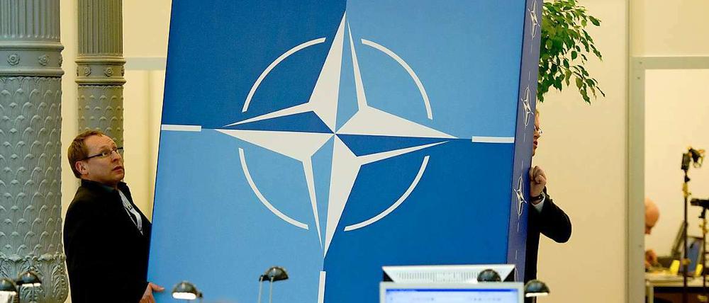 Wohin bloß? Mitarbeiter des Auswärtigen Amtes tragen ein Schild mit dem Nato-Logo durch das Pressezentrum.