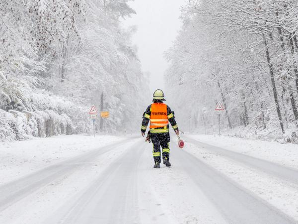 Ein Feuerwehrmann sperrt die Landstraße in Richtung Großer Feldberg wegen eines Schneebrucheinsatzes im Taunus.